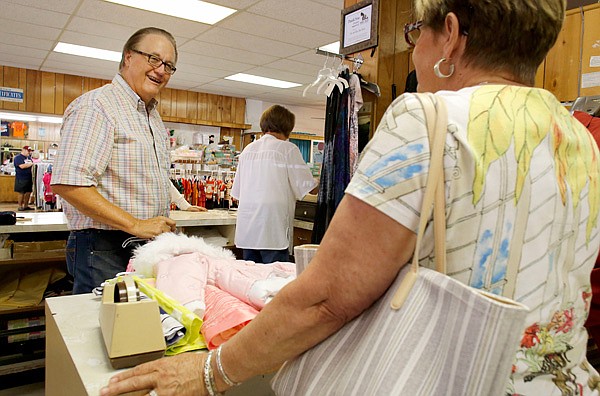 Max Ryan, left, turns to assist customers Friday at the register of his store, Ryan’s, at the corner Emma Avenue and Spring Street in Springdale. The retailer is retiring and closing the store by September after selling off the inventory. 