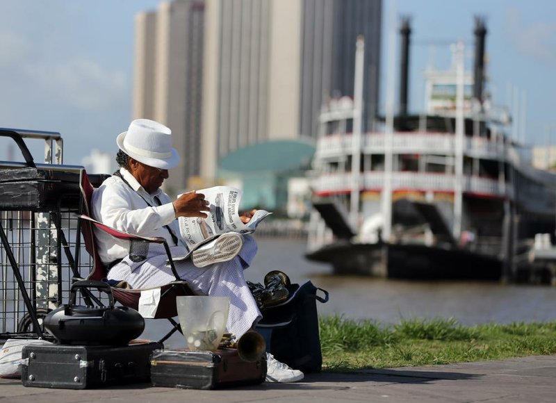 Special to the Arkansas Democrat Gazette - 06/25/2013 - Street musician T.S. Lark reads a copy of the new Times-Picayune Street edition Tuesday morning, June 25, 2013, on the Mississippi River park near the New Orleans French Quarter.  A year ago, The Times-Picayune laid off a large part of its staff and began to publish a newspaper just three days a week. Since that time, the Baton Rouge Advocate has ramped up its operation in New Orleans in order to compete with The Times-Picayune, including home delivery seven days a week. A newspaper war has broken out with The Times-Picayune now publishing six days a week to compete with the Advocate. (Photo by Chuck Cook)