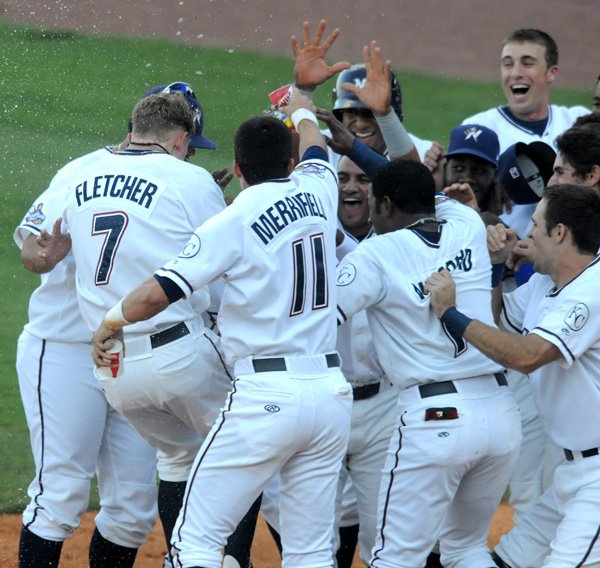 Brian Fletcher, Northwest Arkansas Naturals designated hitter, is greeted by teammates Wednesday at home plate after hitting a two-run game-winning home run in the 11th inning against the Arkansas Travelers at Arvest Ballpark. The home run ended the game, which had been suspended Tuesday night because of rain. 