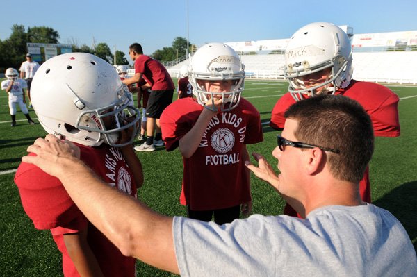 Bryan Clinkscales, bottom, talks to Christian Rock, from left, Braden Conner, and Addison Mick on Thursday at Jarrell Williams Bulldog Stadium in Springdale during the first day of the 60th annual Springdale Kiwanis Kids Day Football game. 