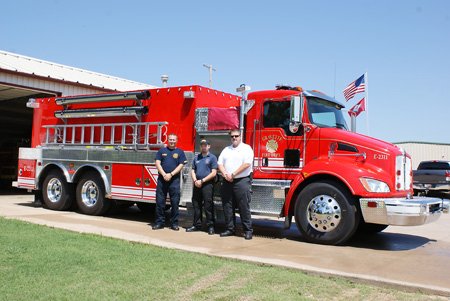 Gravette firefighters, from the left, Robert Douthit and Spencer Gillming, and Fire Chief David Smith stand in front of the new combo pumper/tanker the department received from the county last week. Transfer of hoses, tools, etc., from the two trucks the new rig is replacing has been completed. 