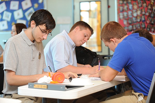 Egan Meaux, 18, left, works on an essay Wednesday alongside Harper Grimsley, 16, and Levi Pruett, 16, during an environmental science class at Haas Hall Academy in Fayetteville. 