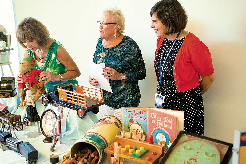 Quester members Mary Ellen Gardner, from the left, and Beth Goeden present a collection of vintage toys to Sarah McClure, librarian and manager of the Hillary Rodham Clinton Children’s Library & Learning Center in Little Rock.