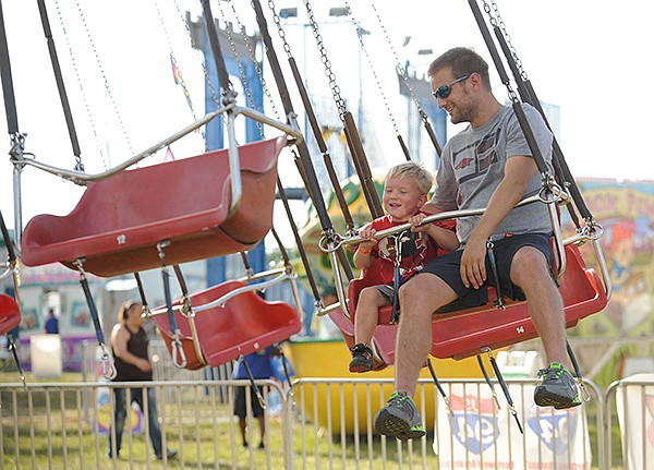 STAFF PHOTO ANDY SHUPE - Brad Watts of Fayetteville, right, laughs with his 3-year-old son, Ethan Watts, as they ride the Lolliswing Wednesday, Aug. 28, 2013, at the Washington County Fair in Fayetteville.