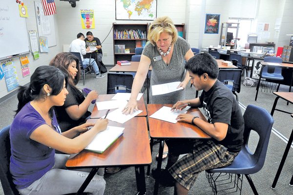 Candis Harrell, teacher at Har-Ber High School, hands out an assignment Wednesday to juniors, from left, Viviana Contreras, 15, Milvia Linares, 17, and Theodor Peren, 17, in her critical reading class at the school in Springdale. 