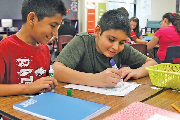 Junior Garcia, left, smiles Friday as Arbran Duran makes his move in a math activity in Jean Ogden’s sixth-grade class at Oakdale Middle School in Rogers. A district math makeover in sixth grade this year puts more emphasis on learning concepts through activities.