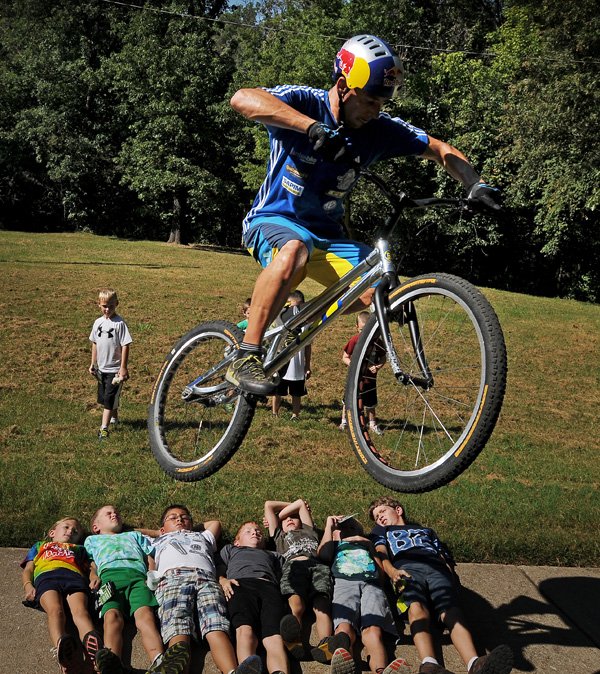 Professional trials rider Kenny Belaey, from Belgium, hops his bike over children from local elementary schools on Thursday September 5, 2013 during the Slaughter Pen Jam media preview event at Park Spring Park in Bentonville. Trials riders will descend on the Bentonville square on Friday for an exhibition of the relatively new sport in which riders attempt to bounce, hop and balance over various obstacles.