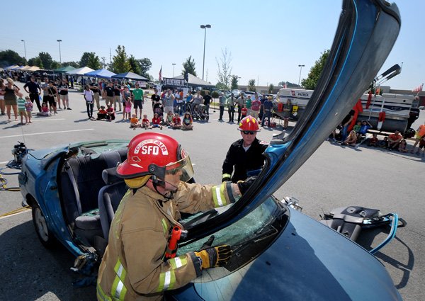 Springdale firefighter Rick Bostian, left, and Amkus Rescue Systems rep Dean Deterts demonstrate how Amkus hydraulic rescue tools are used to cut open a car during Patriot Day, Sponsored by Sheep Dog Impact Assistance, on Promenade Boulevard near Target in Rogers on Saturday September 7, 2013.