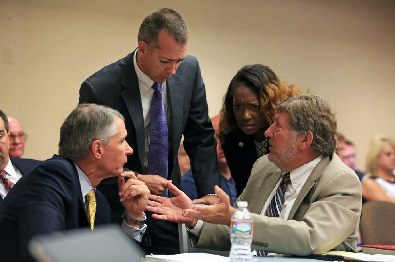 Jay Bequette (left), attorney for the Clarksville School District, and Scott Hickam (right), attorney for the Lake Hamilton School District, confer with Warren Readnour and KaTina Hodge of the attorney general’s office Wednesday during licensing hearings. 