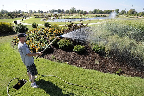 Mark Jeffery with the Bentonville Parks and Recreation Department waters the greenery in July 2012 in the flower beds at Orchards Park in Bentonville. City workers started the groundwork for Legacy Orchards at the park on Northeast J Street this week.