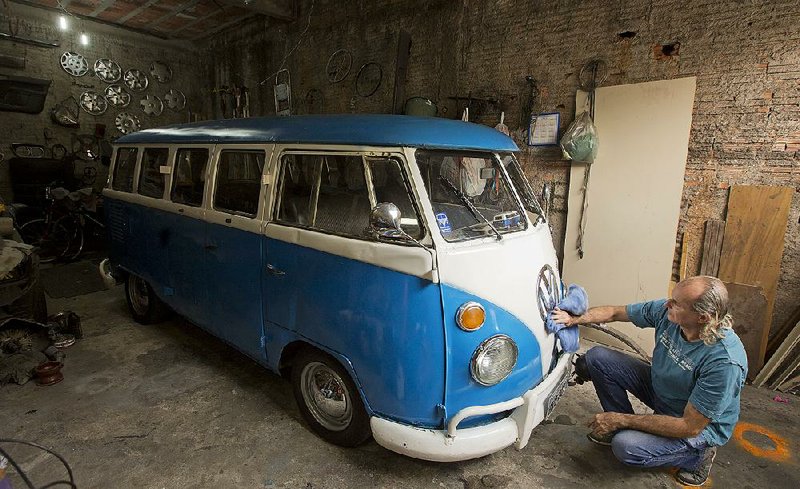 In this Sept. 16, 2013 photo, Enio Guarnieri wipes the VW emblem of his 1972 Volkswagen van, in Sao Paulo, Brazil. Guarnieri, who keeps his blue and white van or Kombi in his cluttered garage, bought the vehicle a year ago to stoke childhood memories. When he was 10, his father taught him to drive a Kombi. "Driving a Kombi with your face up against the windshield is a thrilling adventure, there is no other van like it," he said. "There is no other van that is so easy and inexpensive to maintain. Anyone with a minimum amount of knowledge about engines and a few tools can fix a Kombi." (AP Photo/Andre Penner)