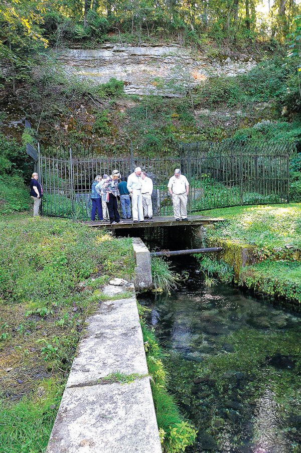 Officials with the Arkansas Game & Fish Commission and Illinois River Watershed Partnership gaze Wednesday at clear spring water spilling from a cave entrance in Cave Springs where Game & Fish will build education facilities and possibly a regional office. About 50 Game & Fish and partnership representatives toured the 30-acre site that was formerly Lake Keith. 