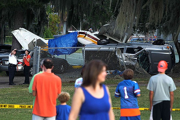 Gator fans gather around police tape to watch the scene of a small plane crash on Flavet Field on the campus of the University of Florida on Saturday, Oct. 5, 2013 in Gainesville, Fla. Two people are hospitalized after a small plane towing a banner crashed near tailgaters gathered for the Florida football game against Arkansas. (AP Photo/The Gainesville Sun, Matt Stamey) 