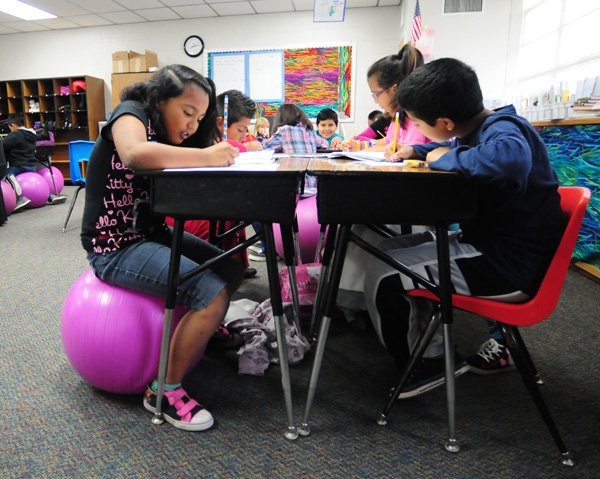 Kyra Guzman, 8,  left, sit with other classmates on yoga ball while Jack Salinas, 8, sits in a chair while doing work in Jennifer Mills 3rd grade class at Jones Elementary School in Springdale. Schools has been using yoga balls, bands on chair legs, seat cushions and stationary bikes to help fidgety students focus during class. The yoga balls also help them have good posture because it makes it hard for the kids to slouch or lean.