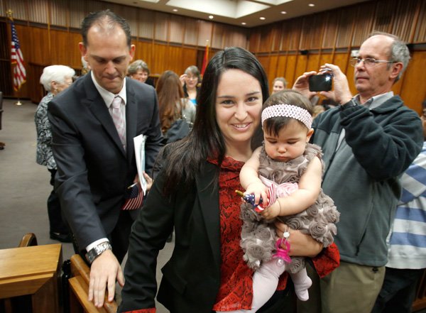 Laerte Voss (left), follows his wife Diani Voss and daughter Nina, seven months, all of Brazil, after receiving certificates and flags Friday morning Oct. 25, 2013 following the United States District Court Western District of Arkansas Naturalization Proceedings in the John Paul Hammerschmidt Federal Building in Fayetteville. The Voss's were two of 36 persons from 15 countries took the Oath of Allegiance and were sworn in as citizens of the United States.