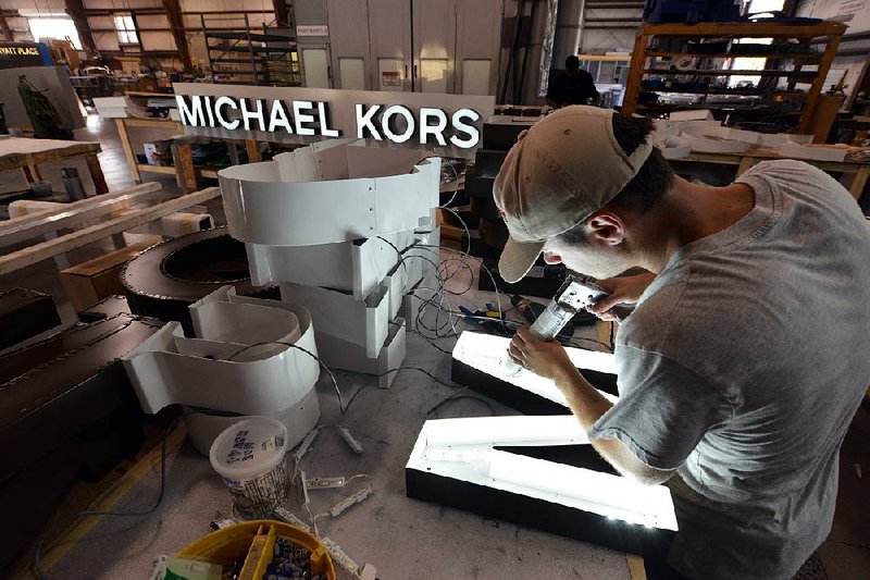 Michael Bresee applies adhesive to LED lights inside letters for a Michael Kors sign at Baron Sign Manufacturing in Riviera Beach, Florida, U.S., on Tuesday, Oct. 21, 2013. Manufacturing unexpectedly picked up in September, showing American factories were a source of strength for the worldís largest economy. Photographer: Mark Elias/Bloomberg *** Local Caption *** Michael Bresee