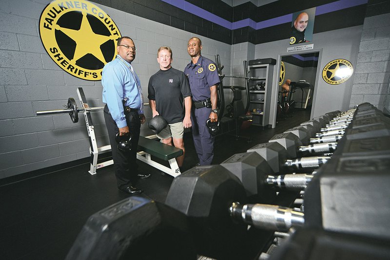 From the left, Maj. John Randall, John Blasioli and Lt. Durwin Lasker stand in the new Hans J. Fifer Exercise Facility at Unit 2 of the Faulkner County Detention Center in Conway. Randall, Lasker and Lt. Todd Mize talked about how to honor Fifer, who died during training, and they came up with the idea of a workout area. Blasioli, Fifer’s father-in-law, raised the money for all of the equipment. A photo of Fifer hangs prominently in the space.