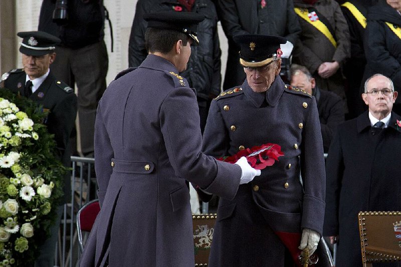 Britain's Prince Philip, , center, is handed a wreath to lay during a special Armistice Day ceremony under the Menin Gate in Ypres, Belgium on Monday, Nov. 11, 2013. The Duke of Edinburgh attended a special Armistice Day ceremony on Monday to oversee the handover of 70 sandbags of soil from Flanders fields. The sandbags, collected by Belgian and British schoolchildren from Commonwealth cemeteries in Belgium, were handed over to the King's Troop Royal Horse Artillery and will be taken to London and placed in the Flanders Fields Memorial Garden at the Wellington Barracks. (AP Photo/Virginia Mayo)