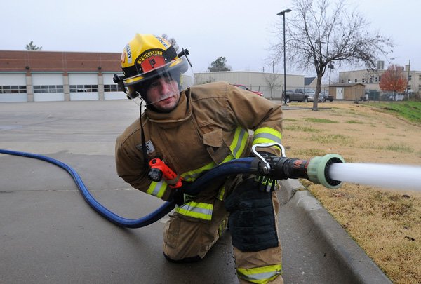 Lawson Osburn, probationary firefighter with the Springdale Fire Department, runs water through a hose Friday, Nov. 22, 2013, during a Driver/Operator test at Station 1 in Springdale. New fire house designs and relocation costs are proving to be too expensive for the department to afford.