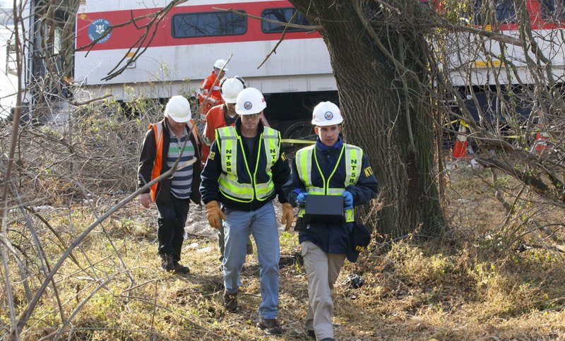 In this Dec 1, 2013, photo provided by the National Transportation Safety Board, safety board investigators Mike Hiller, center left, and George Haralampopoulous, right, walk with an data recorder retrieved from the derailed Metro-North train in the Bronx borough of New York. Two data recorders from the commuter train that derailed while rounding a riverside curve, killing four people, may provide information on the speed of the train, how the brakes were applied and the throttle setting, a member of the NTSB said Monday, Dec. 2, 2013. 