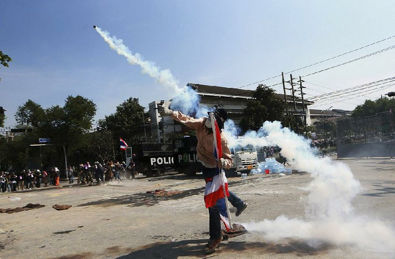 An anti-government protester throws back a tear gas canister fired by riot police near the Government House in Bangkok, Monday, Dec. 2, 2013. Thailand's Prime Minister Yingluck Shinawatra said Monday she is willing to do anything it takes to end violent protests against her government and restore peace, but cannot accept the opposition's "unconstitutional" demand to hand power to an unelected council. (AP Photo/Wason Wanichakorn)