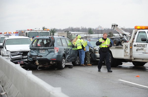 Cpl Preston Oswalt of the Fayetteville Police Department assists tow truck drivers Thursday, Dec. 5, 2013, in collecting one of seven cars involved in a collision on Interstate 540 at the Porter Road exit in Fayetteville.
