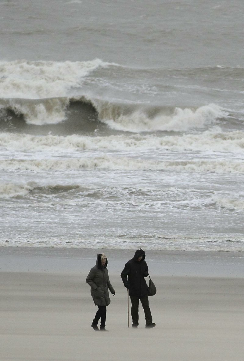 People walk on the beach during stormy weather Thursday in the coastal town of Blankenberge, Belgium. 