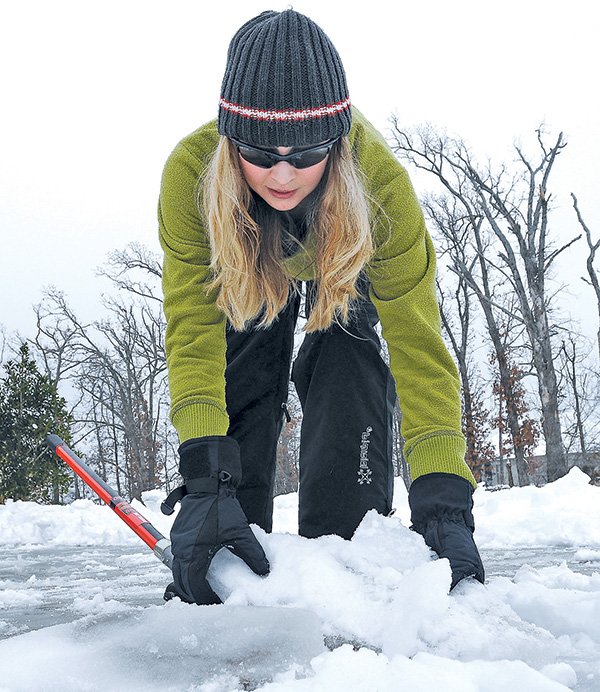 STAFF PHOTO SAMANTHA BAKER 
• @NWASAMANTHA 
Ashley Mason picks up a block of ice from her driveway Sunday at her home in Springdale. Mason was out shoveling her driveway which was mostly packed with ice.