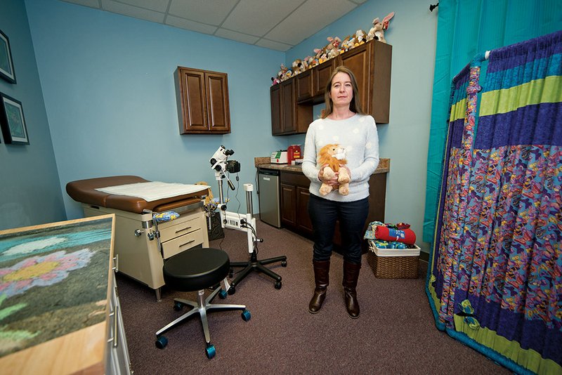 Tess Fletcher, executive director of the Children’s Advocacy Alliance of North Central Arkansas, holds a stuffed animal in the new medical-exam room in the Central Arkansas Children’s Advocacy Center, 707 Parkway St. in downtown Conway. The room was made possible by a piece of equipment, left, called a colposcope, which was purchased by the Conway Regional Health Foundation. Fletcher said the instrument allows for noninvasive exams of children who are suspected to have been sexually abused. An open house is set for 2-4 p.m. Sunday.