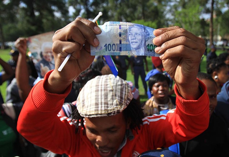 A well-wisher holds up a 100 rand bill bearing the image of Nelson Mandela on Wednesday after the former South African president’s body passed by in a procession to the Union Buildings in Pretoria where it is to lie in state. 