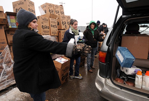 Volunteers Lisa Sizemore, from left, Colleen Weigle and Tasha Wilson toss tissues and paper towels into vehicles as families arrive to pick up Christmas presents from Sharing & Caring of Benton County at the Benton County Fairgrounds in Bentonville on Friday December 13, 2013.
