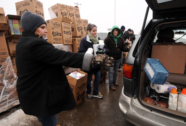 Volunteers Lisa Sizemore, from left, Colleen Weigle and Tasha Wilson toss tissues and paper towels into vehicles as families arrive to pick up Christmas presents from Sharing & Caring of Benton County at the Benton County Fairgrounds in Bentonville on Friday December 13, 2013.