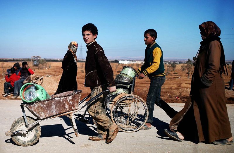 A Syrian refugee boy uses a wheelchair to transport gas cylinders in front of the Norwegian Refugee Council's (NRC) distribution center, at Zaatari refugee camp, near the Syrian border in Mafraq, Jordan, Monday, Dec. 16, 2013. NRC began distributing stoves to Syrian refugees at the Zaatari camp in Jordan on Monday, as bitter winter weather made living conditions worse. (AP Photo/Mohammad Hannon)