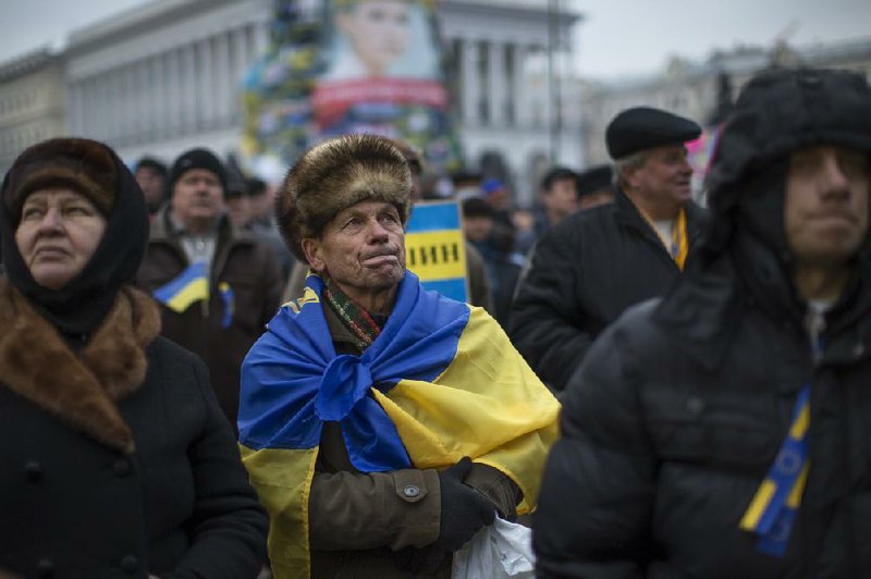 A man wrapped in a Ukrainian national flag listens with other activists to a priest Tuesday during a pro-European Union rally in Independence Square in Kiev, Ukraine. 