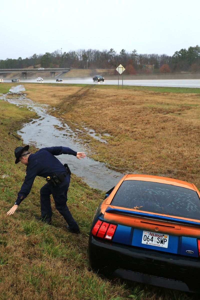 Arkansas Democrat-Gazette/RICK MCFARLAND --12/21/13--  State Police Officer J. Berry slips but is able to catch himself on the wet grass of an embankment after he checked an abandoned vehicle that had slid off I-40 near Burns Park in North Little Rock Saturday. The male driver was not injured and he left in another vehicle before emergency responders arrived. Heavy rains inundated most of the state Saturday.