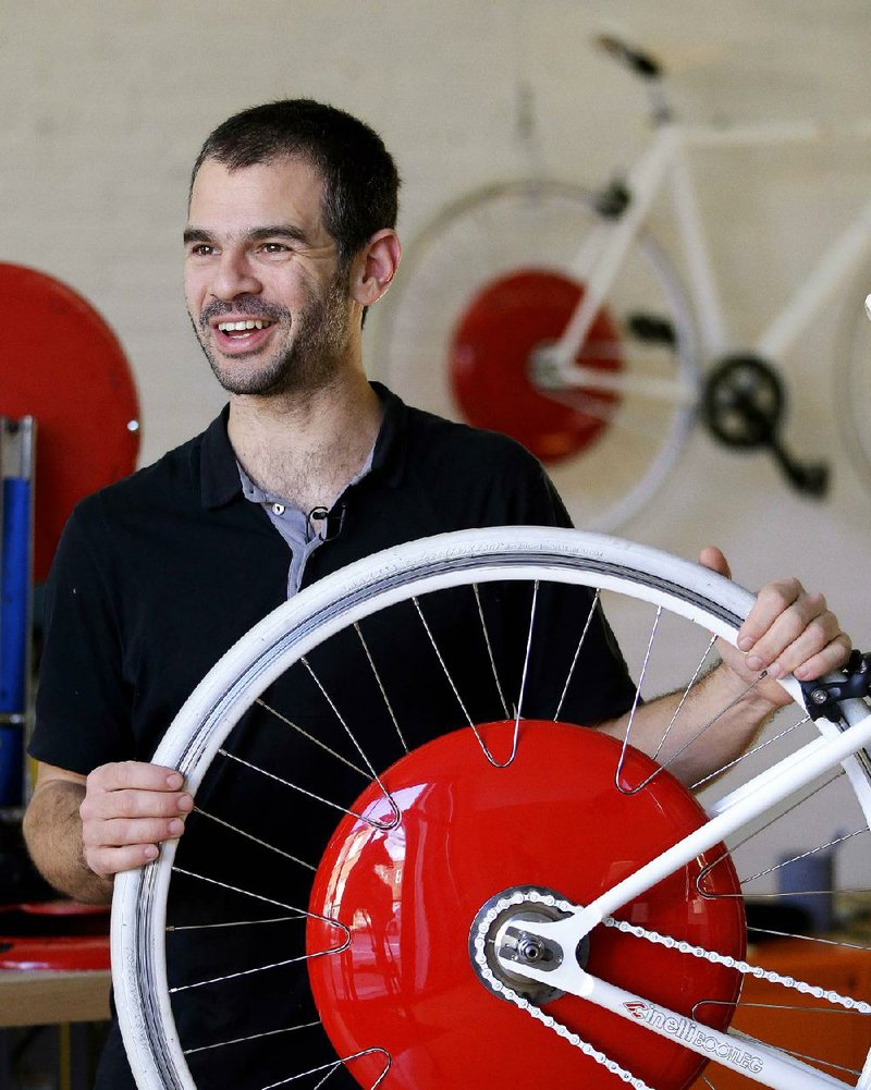 In this Thursday, Dec. 12, 2013 photo, Assaf Biderman, co-inventor of the Copenhagen Wheel and Associate Director of the SENSEable City Laboratory at MIT, poses with his invention at Superpedestrian, his venture-backed company in Cambridge, Mass. The Copenhagen Wheel is a human/electric hybrid bicycle engine built into a bicycle's back wheel. Pre-orders for the Copenhagen Wheel are being taken with delivery expected by May 2014. (AP Photo/Stephan Savoia)