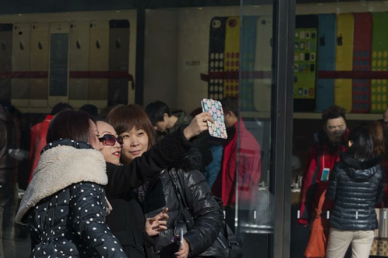 Chinese women use a non-Apple brand phone to take a photo of themselves outside the Apple retail shop in Beijing Monday, Dec. 23, 2013. Apple and China Mobile announced a long-anticipated agreement Monday to bring the iPhone to the world's biggest phone company. The iPhone, once hugely popular in China, has been eclipsed by the rise of lower-priced rival smartphones from Samsung and Chinese companies. (AP Photo/Ng Han Guan)