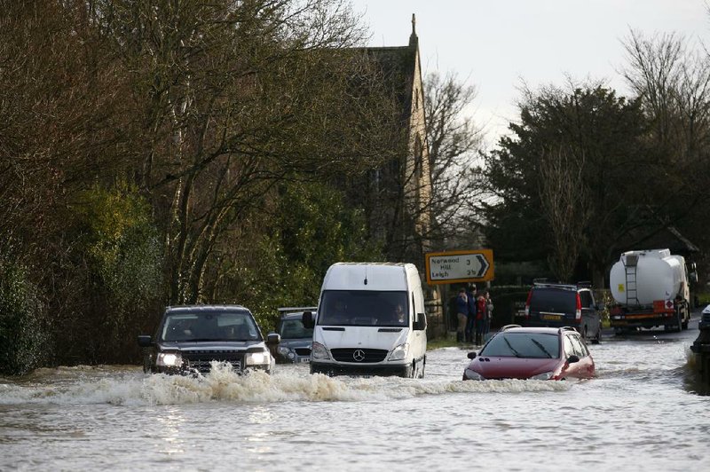 A car tries to drive past stalled vehicles Tuesday on a flooded road near Reigate, England. The winter storm caused major travel delays at Paris and London airports and caused at least five deaths in England and France. 