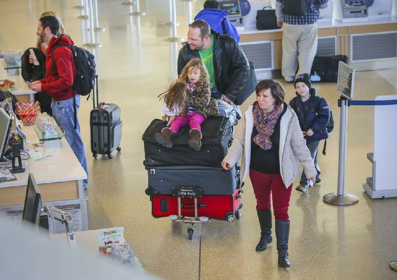 Jock Marx (upper center) wheels a cart of luggage topped off with his daughter, Belle, 4, as they move to a ticket counter with Jock’s wife, Jessica, and son, Talon, 7, Tuesday at Bill and Hillary Clinton National Airport/Adams Field in Little Rock. The family drove from their Memphis home for a cheaper
flight to Oregon to be with family for Christmas. 