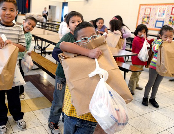 STAFF PHOTO ANTHONY REYES 
Augustine Ishoda, 6, struggles with bags as big as he is Friday at Jones Elementary School in Springdale. Augustine and the other students at the school received Christmas gifts thanks to community donations.