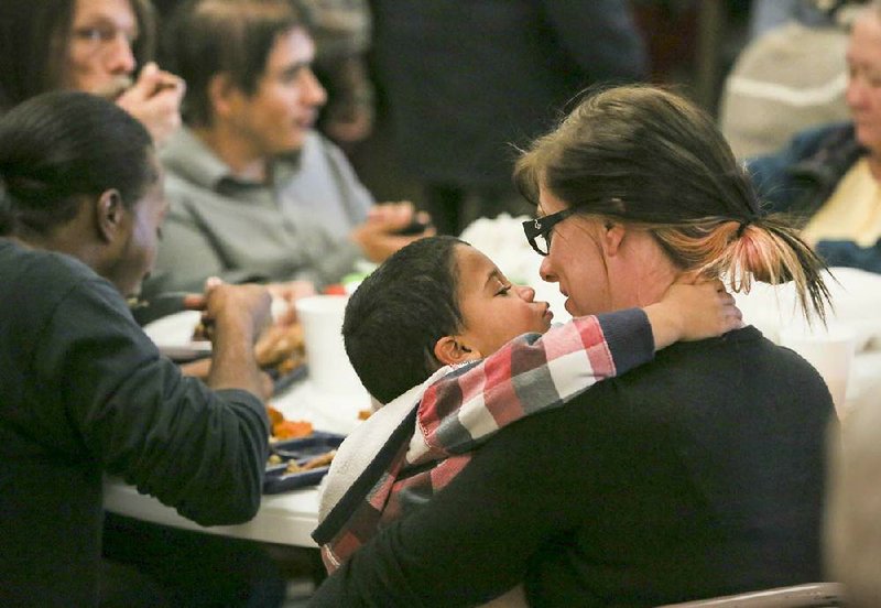 Tara Branstetter gets a smooch from her son Kellen, 2, while they eat lunch with visitors and volunteers during one of three meals served on Christmas Day at the Little Rock Compassion Center. Churches, civic organizations and other groups served thousands of meals across Arkansas on Wednesday. 