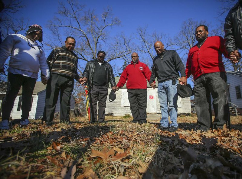 Area pastors pray on Christmas Day with family and friends of a recent shooting victim in front of an abandoned house along West 15th Street in Little Rock. The brother of Jammie Ingram (left) was found slain in a car near West 15th and Abigail streets early Monday. Also pictured (beside Ingram, from left) are Lloyd Craighead, Homer Fairchild Sr., Marcus Wiggins, Darryl White and Milton Graham. 