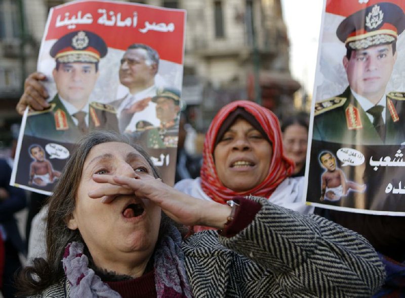 An Egyptian activist shouts slogans as others hold posters showing Defense Minister Gen. Abdel-Fattah el-Sissi, left on the poster, and late President Gamal Abdel-Nasser, with the Arabic that reads, "Egypt is entrusted to us. The army and people are one hand," during an anti-terrorism demonstration in Cairo, Egypt, Thursday, Dec. 26, 2013. A bomb blast hit a public bus in the Egyptian capital, wounding several people, the Interior Ministry said, in an attack that raised concerns that a wave of violence blamed on Islamic militants that has targeted security forces and military for months is increasingly turning to hit civilians. (AP Photo/Amr Nabil)