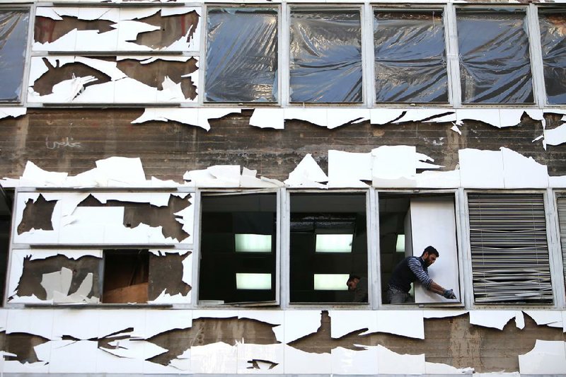 A worker cleans shattered glass from broken windows at a damaged business center, at the scene of an explosion, in central Beirut, Lebanon, Friday, Dec. 27, 2013. A powerful car bomb tore through a business district in the center of the Lebanese capital Friday, killing a prominent pro-Western politician and at least five other people in an assassination certain to hike sectarian tensions already soaring because of the civil war in neighboring Syria. (AP Photo/Hussein Malla)