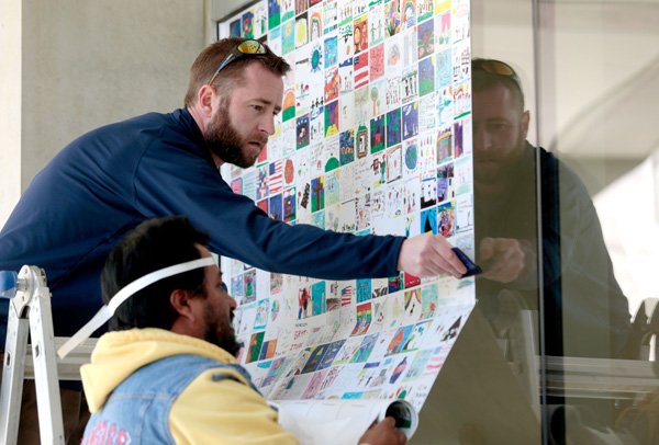 Justin Lantz (cq) and Roy Martinez (near), both with AMP Sign & Banner, install artwork on the doors of the education area at Crystal Bridges Museum of American Art on Friday, Dec. 27, 2013, in Bentonville. The collection is comprised of 6,000 pieces of art created by students in Bentonville Public School and visitors through the museum. Through the Everyartist Live! project, students created the art on the theme of "gratitude."