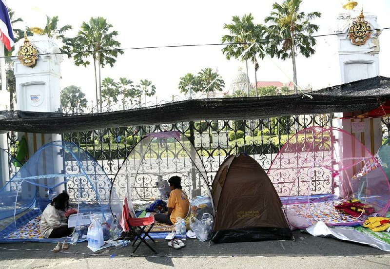 Thai anti-government protesters do their morning duty inside mosquito's nets at a makeshift camp where their colleagues were shot outside the prime minister's office of Government House, background, Saturday, Dec. 28, 2013 in Bangkok, Thailand. Gunmen killed an anti-government protester and wounded two others in the Thai capital on Saturday, raising fears that the country's deepening political crisis was headed toward sustained violence on the streets of Bangkok. (AP Photo/Apichart Weerawong)
