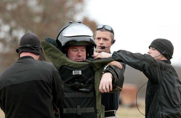 Cpl. Josh Carlson (left), Sgt. Luke Rosebaugh (right) and Cmdr. Michael Meadors help Cpl. Kerry Pippin (second from left) put on a blast suit on Thursday, Dec. 19, 2013, during a training exercise for the Bentonville Bomb Squad at an abandoned house in north Bentonville.