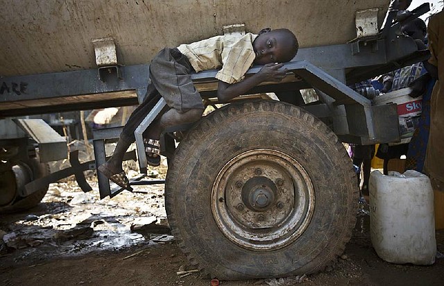 A displaced boy rests Tuesday on the wheel arch of a water truck while others fill containers from it at a United Nations compound on the outskirts of Juba, South Sudan. 