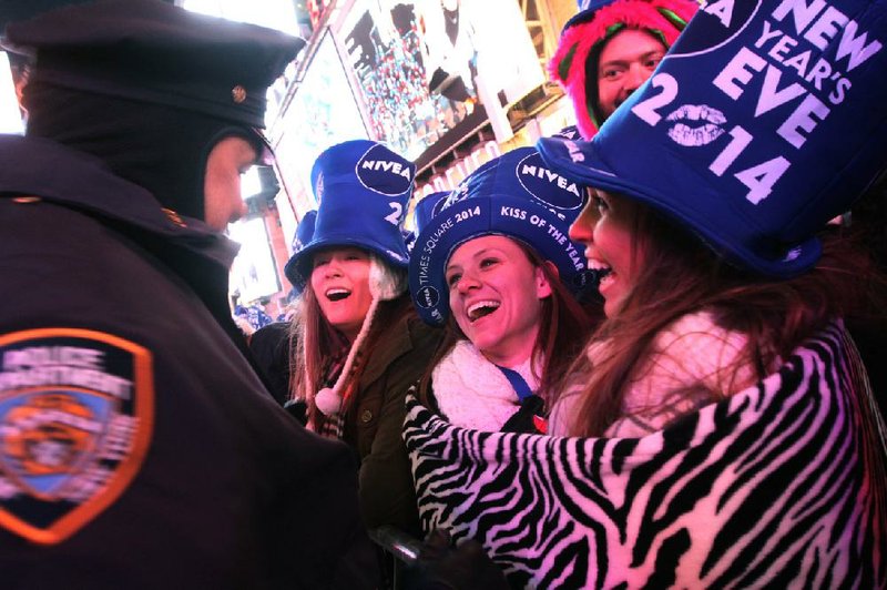 New Year’s revelers keeping warm in a blanket laugh with a police officer Tuesday night in New York City’s Times Square as they await the dropping of the crystal ball to usher in 2014. 