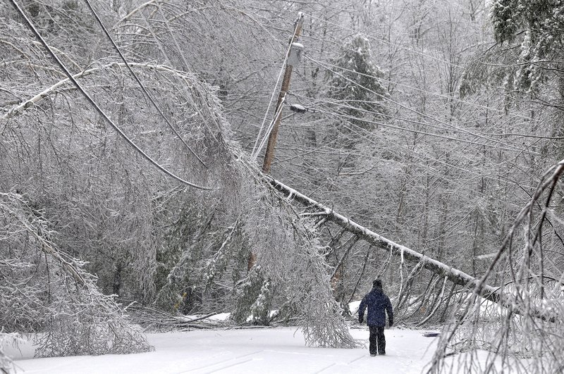 Karen Gibbs walks through a labyrinth of icy broken trees and downed power lines to her home on Maplehurst Drive in Belgrade, Maine on Thursday. Southeast Maine and parts of the state's interior that have been without electricity since Sunday anticipated 3 to 7 inches of snow by the time the latest system pushed off the coast Thursday night. Utilities worried that the additional weight on branches and transmission lines could cause setbacks in the around-the-clock efforts to restore power.